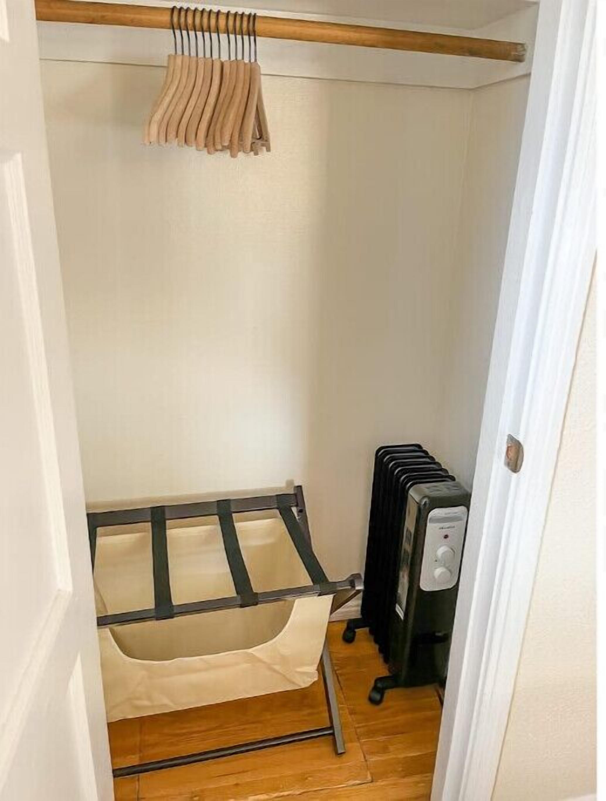 A compact room with a bed, a radiator, and a wooden shelf with hanging items.