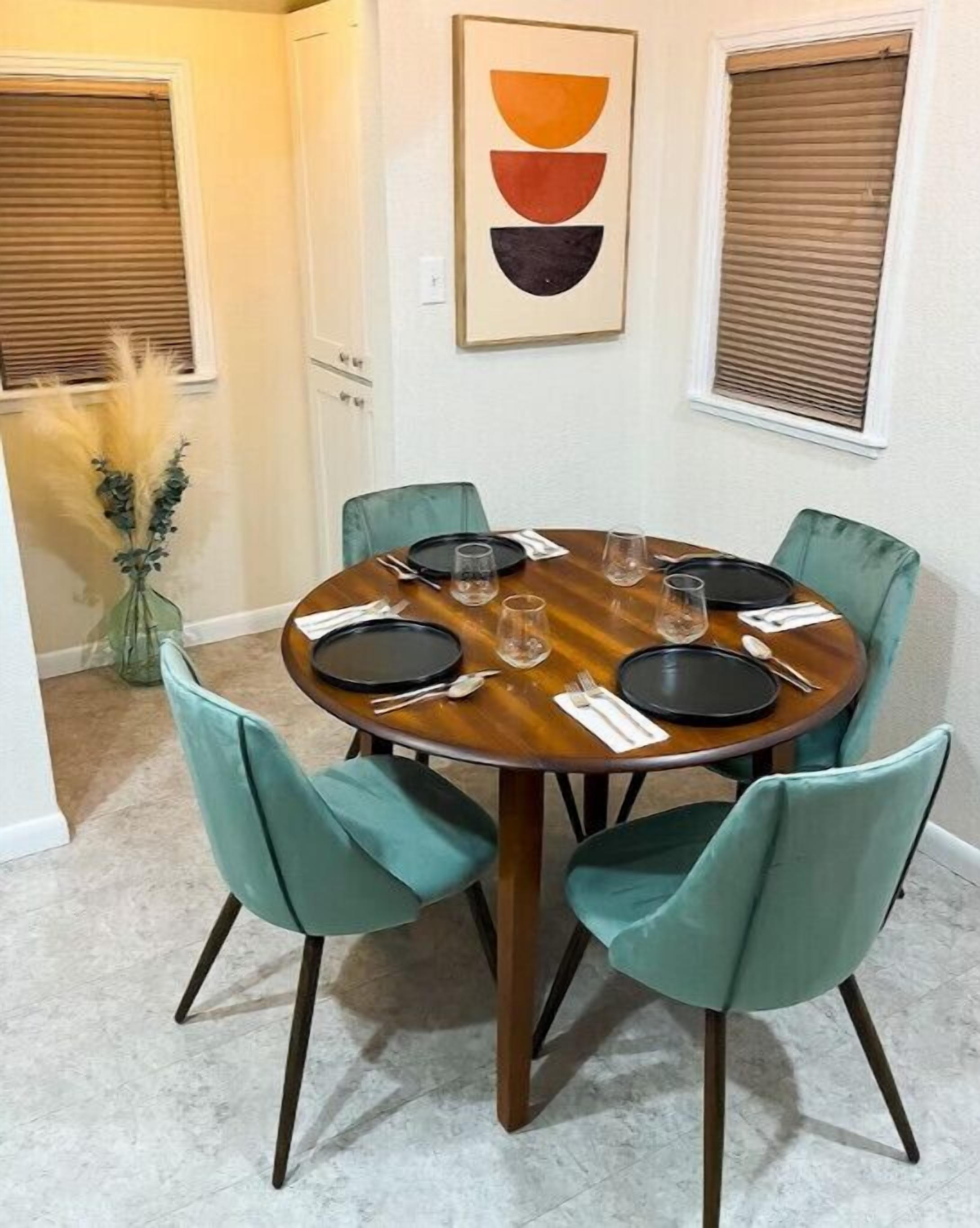 Un coin repas avec une table ronde, six chaises de couleur turquoise et un vase rempli de plumes d’herbe de la pampa.