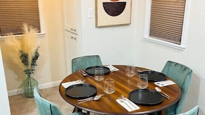 Un comedor con una mesa redonda, seis sillas color turquesa y un jarrón con plumas de miscanthus.