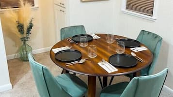 Un coin repas avec une table ronde, six chaises de couleur turquoise et un vase rempli de plumes d’herbe de la pampa.