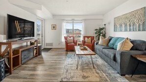 A modern living room with a flat-screen TV, a grey sofa, and a coffee table. - Lakeside Lair | Pool | Hot Tub | A/C (Invermere)