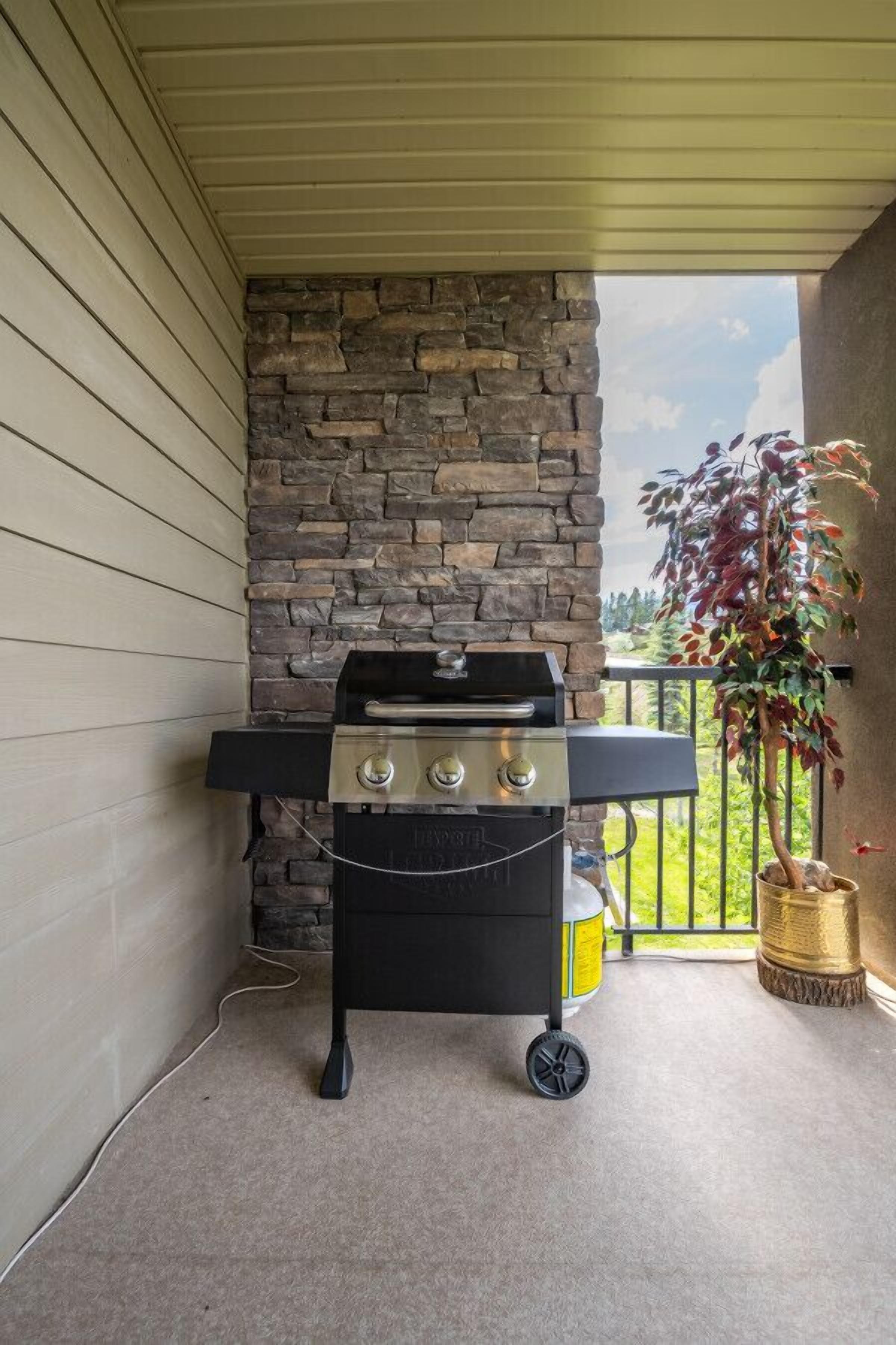 A portable grill on a balcony with a stone wall backdrop and a view of greenery.