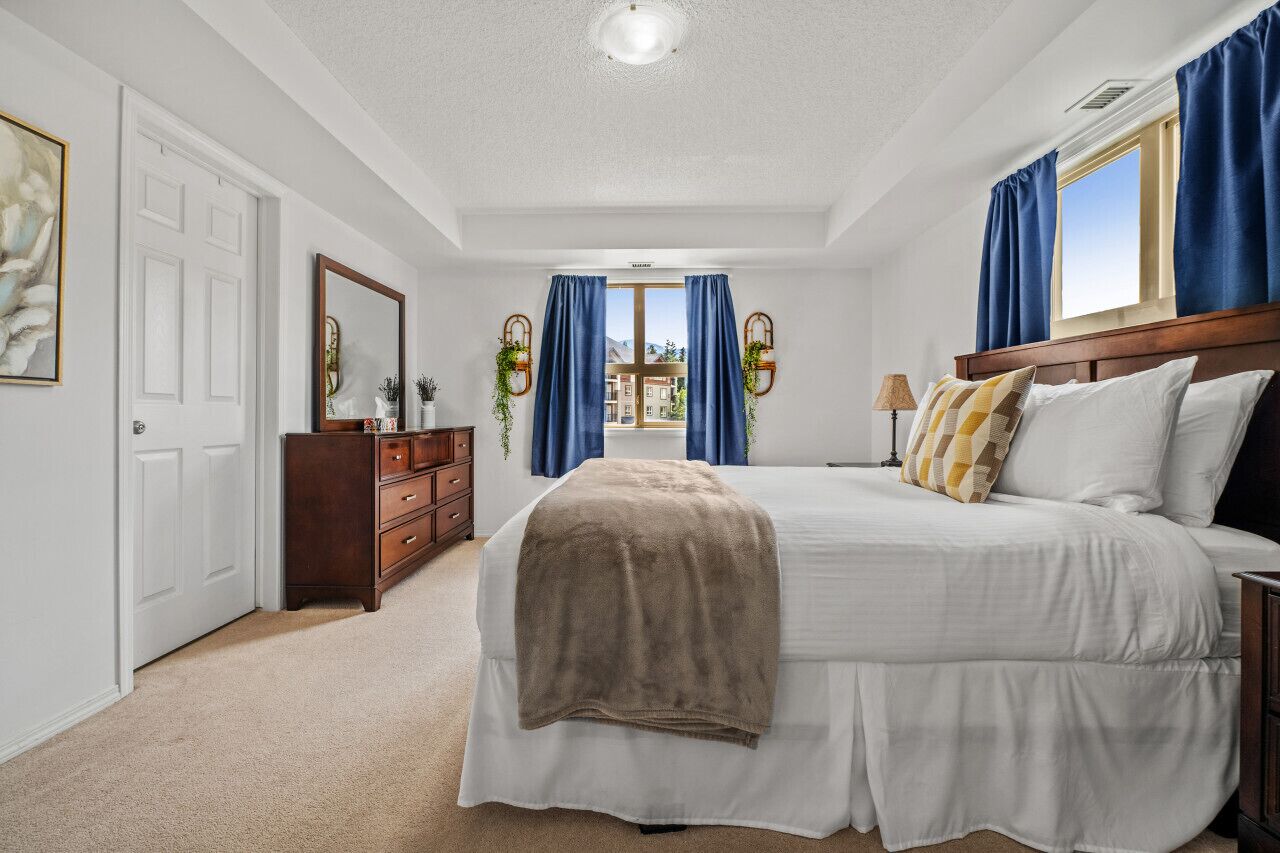 A bedroom with a large bed, a dresser, a mirror, and a window with curtains.