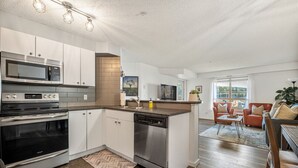 A modern kitchen with stainless steel appliances, a dishwasher, and a dining area with a sofa and coffee table. - Lakeside Lair | Pool | Hot Tub | A/C (Invermere)