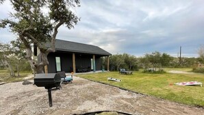A covered outdoor area with a barbecue grill, seating, and a tree. - WunderDog BunkHouse: Ready for FISHing men and women. Privacy for 4! (Rockport)