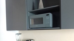 Een compacte kitchenette met een magnetron, een koffiezetapparaat en een blender op een zwart aanrecht.
