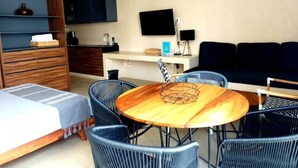 Een moderne woonkamer met een ronde houten tafel, blauwe rieten fauteuils, een bank en een aan de muur bevestigde televisie.
