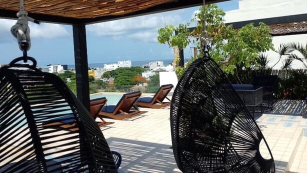 Een overdekt terras met lounge fauteuils en uitzicht op de stad en zee.