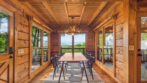 A wooden interior with a large table and chairs, large windows, and a chandelier. - The Maple Bear - Amazing Mountain Views + Hot Tub (Blue Ridge)