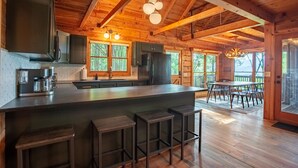 A wooden cabin with a large kitchen island, bar stools, and a dining area with a table and chairs. - The Maple Bear - Amazing Mountain Views + Hot Tub (Blue Ridge)