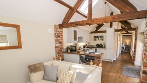 A cozy living room with a sofa and a small bench, a kitchen with a dining area, and a visible bedroom in the background. - The Dairy (Nuneaton)