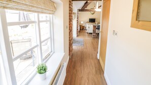 A hallway with a wooden floor, a radiator, a potted plant, and a window with a curtain. - The Dairy (Nuneaton)