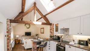 A modern kitchen with white cabinets, a brick accent wall, wooden beams, and a skylight. - The Dairy (Nuneaton)