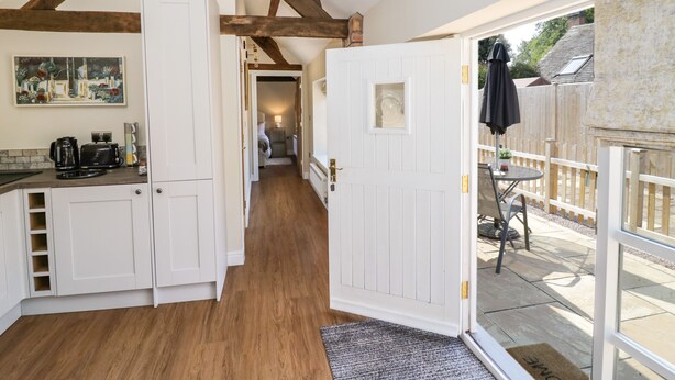 A narrow hallway with wooden beams, white doors, and a kitchen area with appliances. - The Dairy (Nuneaton)
