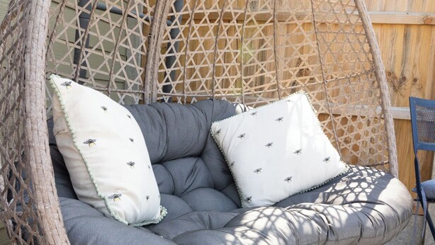 A wicker hanging chair with grey cushions and patterned pillows.
