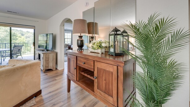 A modern living room with a wooden cabinet, a sofa, a large window, and a potted plant. - Branson Condo Near 76 Strip & Silver Dollar City (Branson)