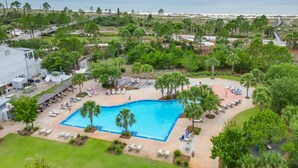 A swimming pool surrounded by palm trees and lounge chairs, with a view of the beach and ocean in the background. - Walk to Beach & Pool: Windmark Beach Home! (Port Saint Joe)