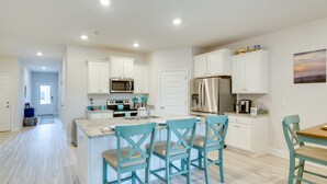 A modern kitchen with white cabinets, a stainless steel refrigerator, and a central island with teal chairs. - Walk to Beach & Pool: Windmark Beach Home! (Port Saint Joe)