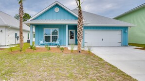 A single-story house with a blue exterior and a white garage door. There are two palm trees in the front yard. - Walk to Beach & Pool: Windmark Beach Home! (Port Saint Joe)