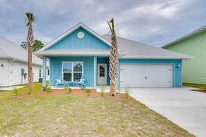 A single-story house with a blue exterior and a white garage door. There are two palm trees in the front yard.
