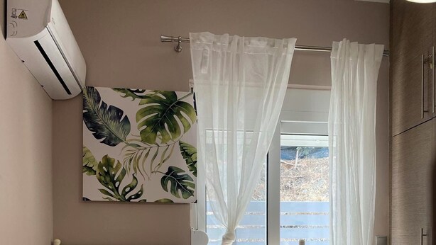 A bedroom with a bed, white curtains, a painting, and a view of the outdoors. - Modern and cozy bungalow, close to traditional villages and airport (Rhodes)
