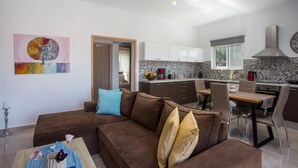 A modern living room with a brown sofa, a dining table, and a kitchen in the background. - Modern and cozy bungalow, close to traditional villages and airport (Rhodes)