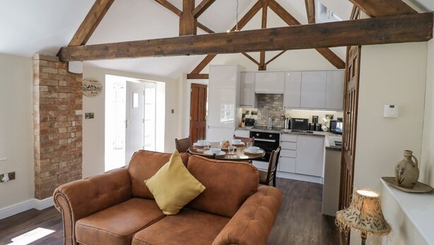 Un salon chaleureux avec un canapé en cuir marron, un plafond en bois et une cuisine à l’arrière-plan.