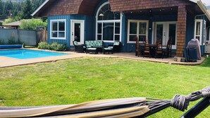 Et hus med en overdækket terrasse, swimmingpool og en græsplæne.