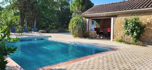 A swimming pool with a tiled deck, surrounded by greenery and a stone building with a tiled roof. - Magnifique mas Privilège en Pleine Nature en Bord de Rivière (Raissac-d'Aude)