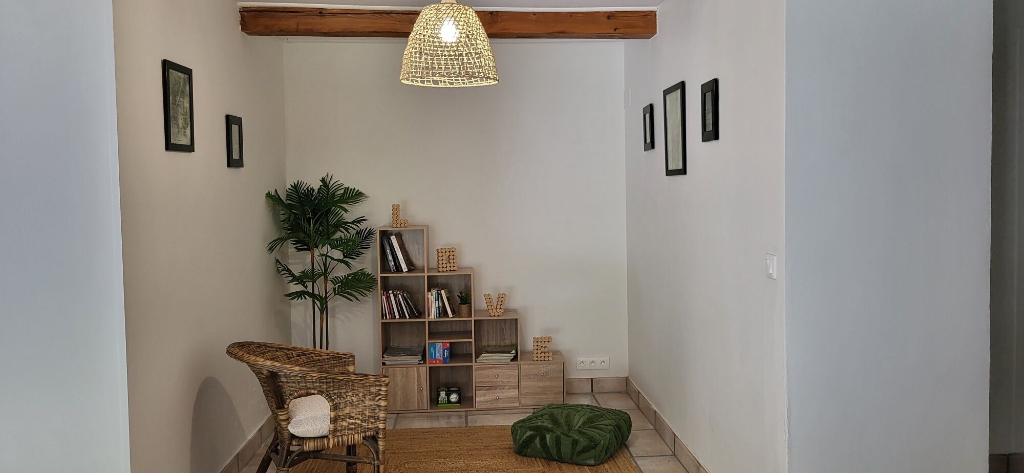 A cozy reading nook with a wicker chair, a bookshelf, and a hanging light fixture.
