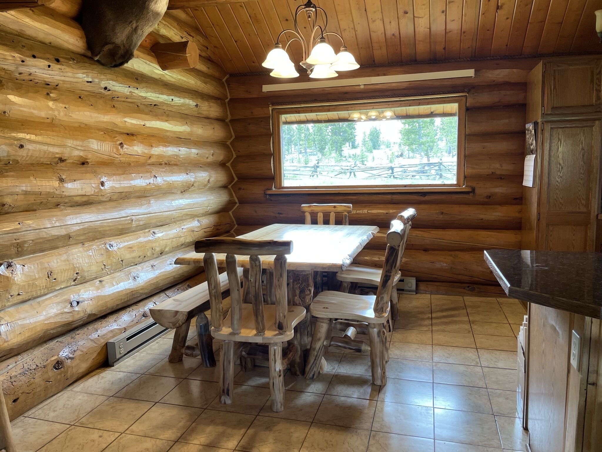 L’intérieur d’une cabane en rondins, avec une table et des chaises en bois, une fenêtre donnant sur les arbres et un coin cuisine doté de meubles en bois.