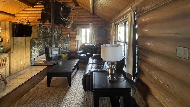 A cozy cabin interior with a stone fireplace, leather sofa, and a ceiling fan. - Stratton Ranch - Wyoming Getaway Cabin - 4 bed/2 bath WY Cabin! (Dubois)