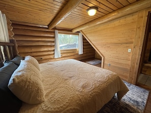 Une chambre confortable dans un chalet, avec un lit, une fenêtre et un plafond en bois.