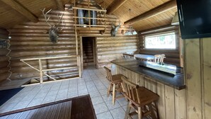 A log cabin interior with a kitchen area, wooden dining table, and chairs. - Stratton Ranch - Wyoming Getaway Cabin - 4 bed/2 bath WY Cabin! (Dubois)