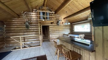 A log cabin interior with a kitchen area, wooden dining table, and chairs.