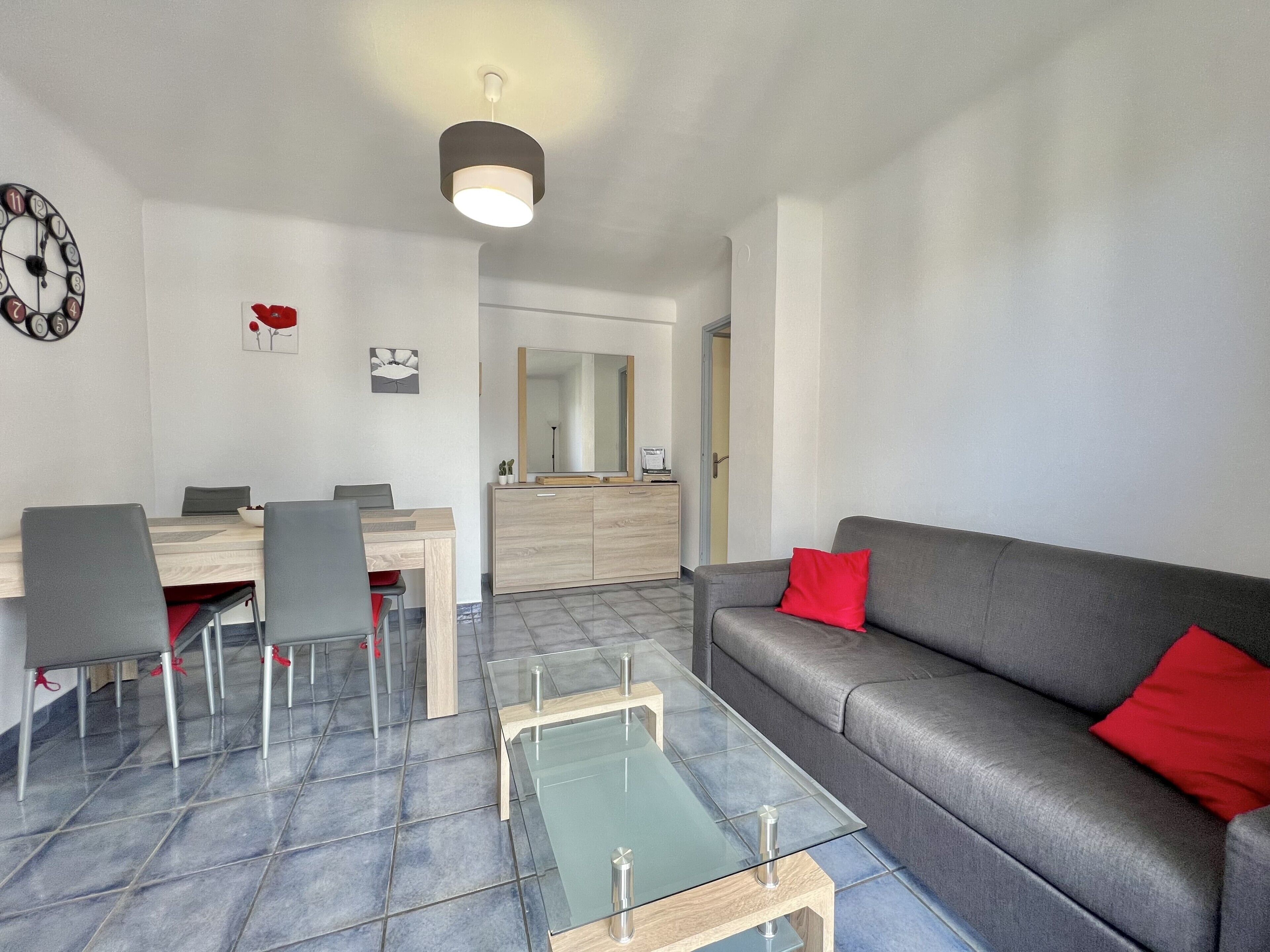 A modern living room with a grey sofa, a glass coffee table, and a dining area with a wooden table and chairs.