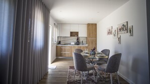 Una cocina moderna con armarios blancos, un revestimiento de pared de madera y una zona de comedor con una mesa de vidrio y sillas grises.