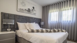 Un dormitorio moderno con una cama grande, una mesita de noche con lámpara y una ventana con cortinas.