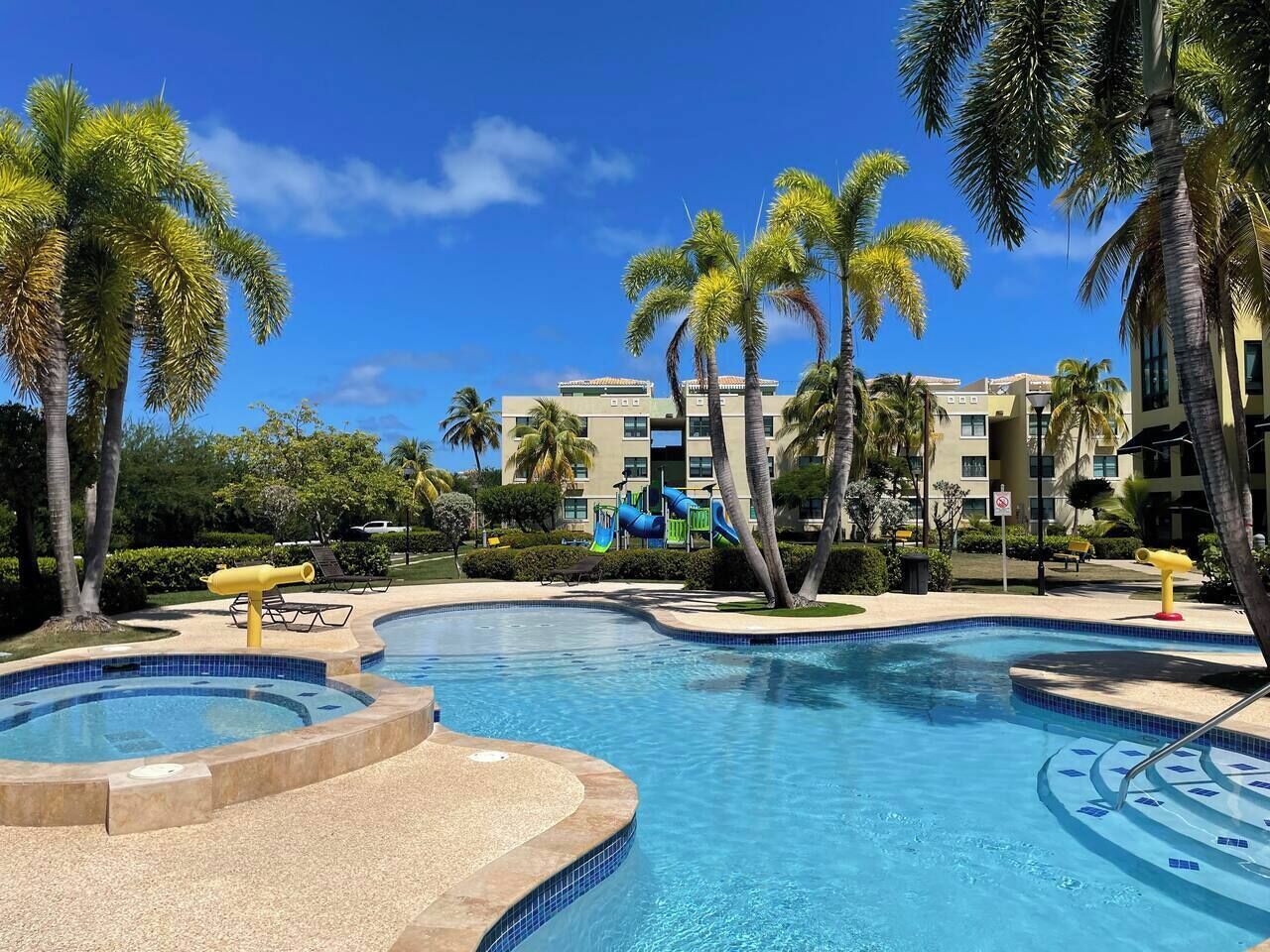 A swimming pool with a slide, palm trees, and a building in the background.