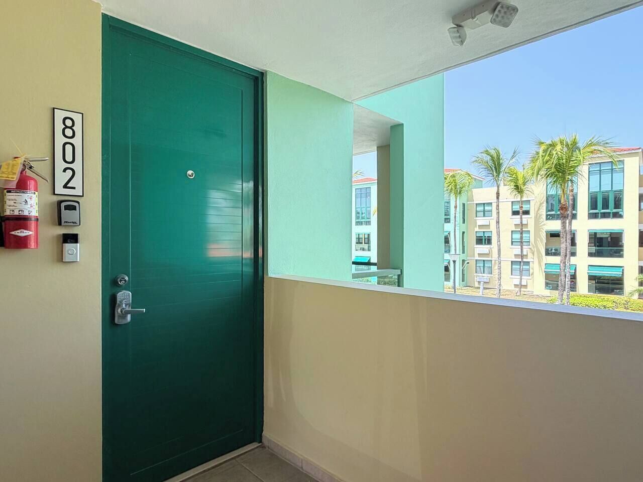 Une porte verte avec une plaque portant un numéro, un extincteur et un dispositif de sécurité fixés au mur.