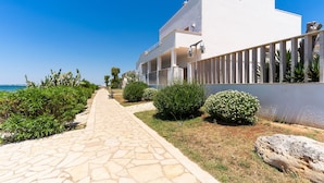 Un chemin menant à un bâtiment moderne à la façade blanche, doté d’un revêtement de sol en pierre et entouré de verdure.