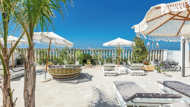 Une terrasse extérieure baignée de soleil, avec des meubles en osier blanc, un espace salon circulaire et des parasols pour créer de l’ombre.