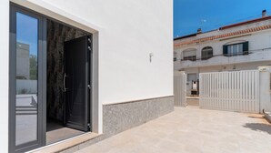 Un bâtiment moderne doté d’une grande porte vitrée, d’un patio carrelé en pierre et d’un mur extérieur blanc.
