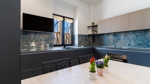A modern kitchen with dark cabinetry, a marble backsplash, and a dining area with a table set for two.
