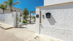 A white building with a gated entrance, a mailbox, and a sign indicating a location.