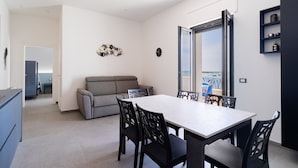 Ein modernes Wohnzimmer mit Essbereich, einem grauen Sofa, einem weißen Tisch und schwarzen Stühlen.
