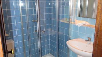 Une salle de bain avec des carreaux bleus, une douche à parois de verre, un lavabo blanc et des toilettes.