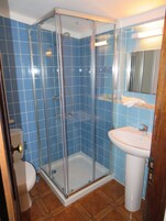 Un baño con azulejos azules, ducha con cerramiento de vidrio, lavamanos blanco y un inodoro.