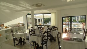 A restaurant with multiple tables and chairs, a buffet area, and large windows offering a view of the outdoors. - Villa Alcaide (Portimão)