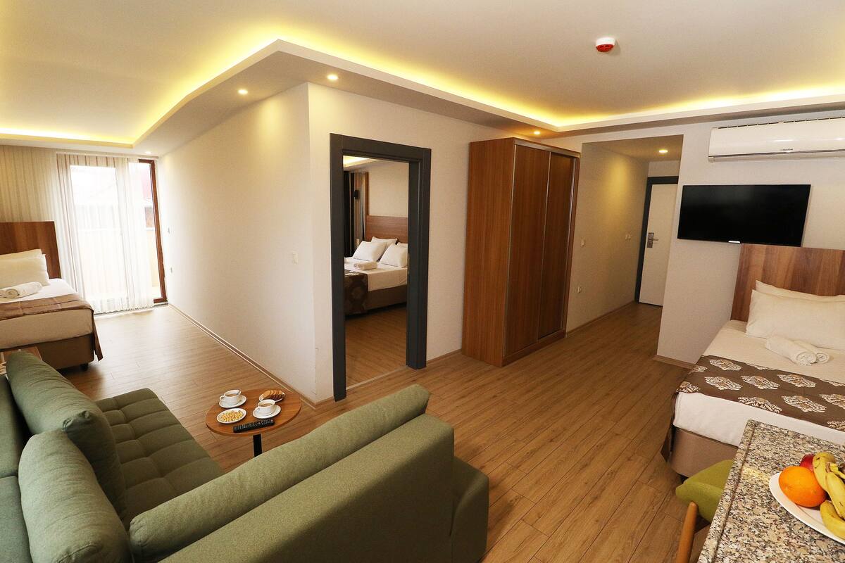 A hotel room with a green sofa, a small table with a fruit plate, a bed with a TV, and a wooden wardrobe.